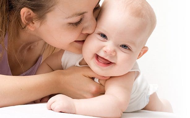 A woman is kissing her baby on the cheek.