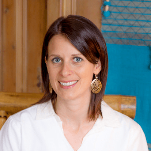 A woman with brown hair wearing white shirt and earrings.