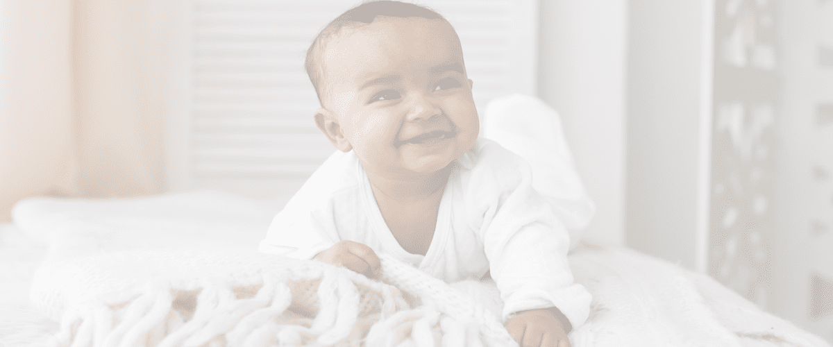 A baby is smiling while laying on the floor.